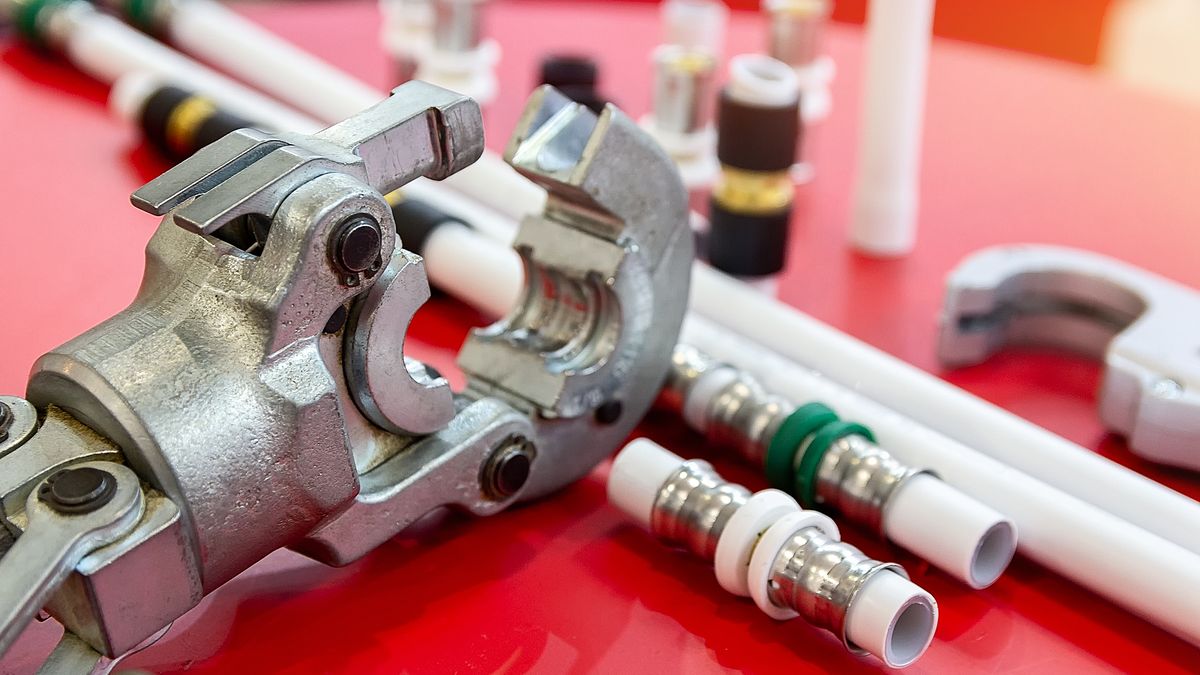 Hand press clamping a press fitting onto plastic supply pipe, more fittings alongside