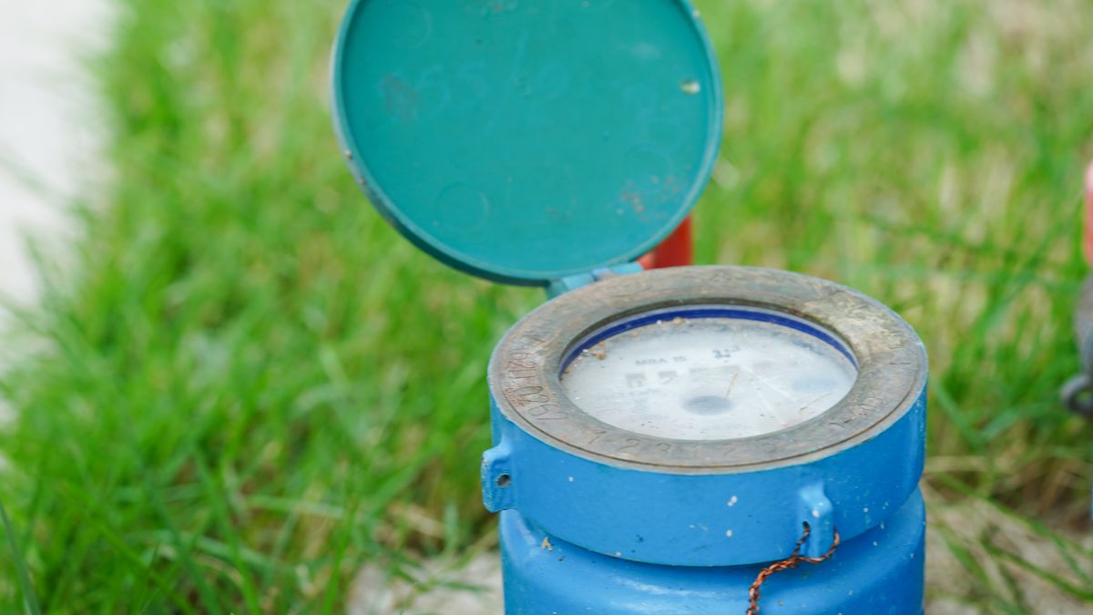 Water meter in a ground chamber with the lid lifted, brass valve alongside